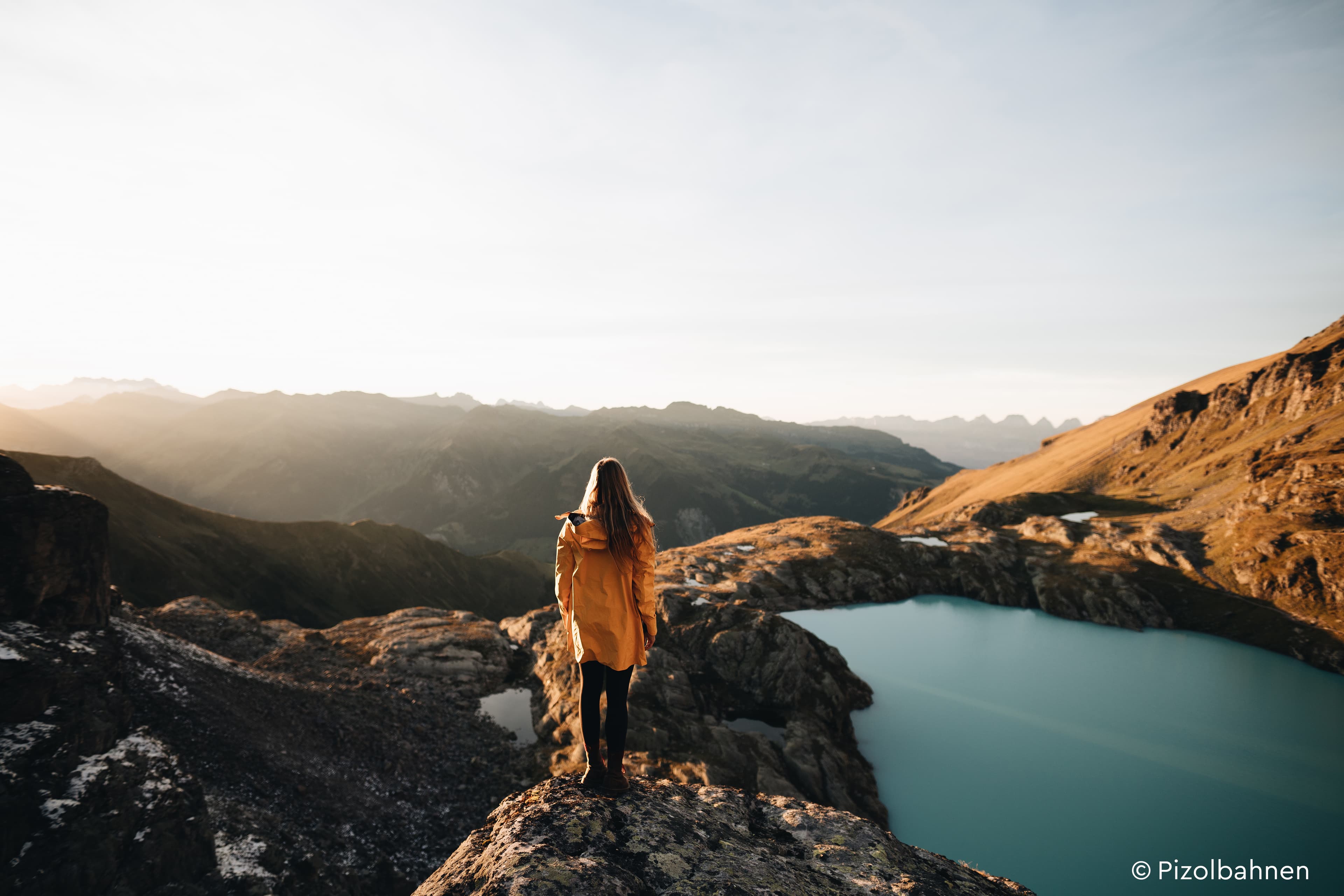 Eine Frau steht auf einem Felsen und schaut auf einen See im späten Sonnenlicht.