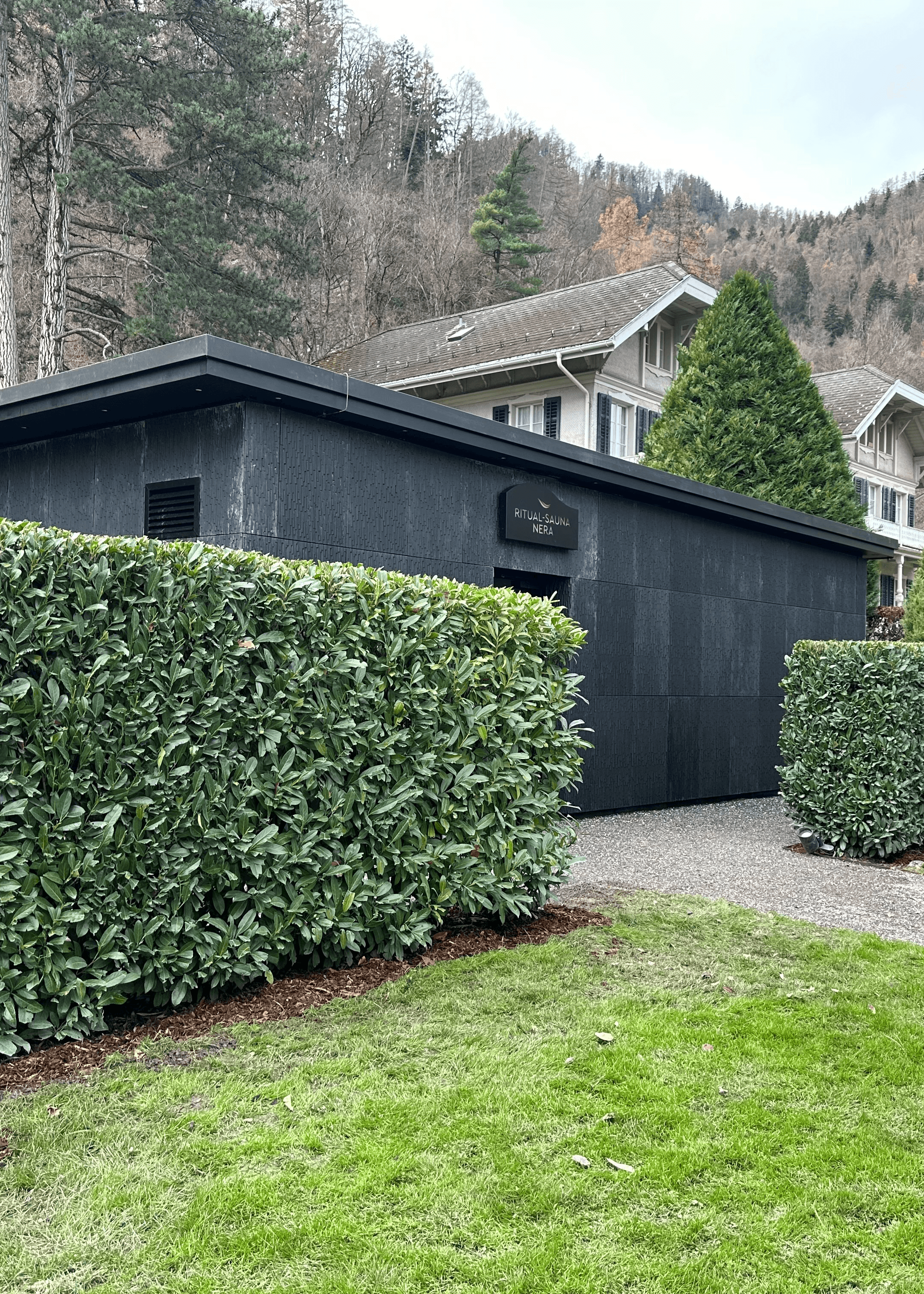 Blick auf ein kleines Häuschen bepflanzt mit einer hohen Hecke.