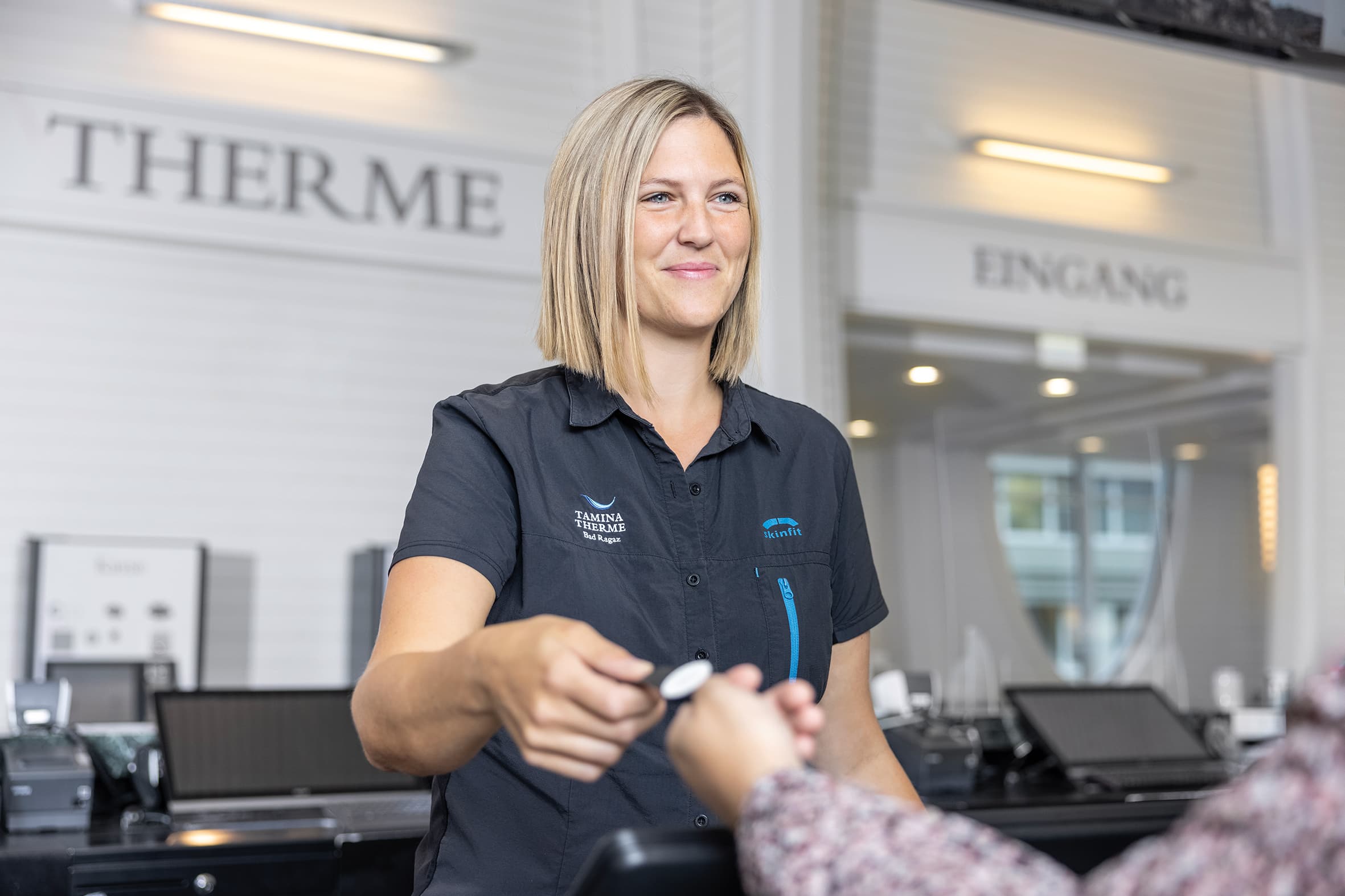 Eine Mitarbeiterin am Empfang der Tamina Therme übergibt einem Gast einen Schlüssel.