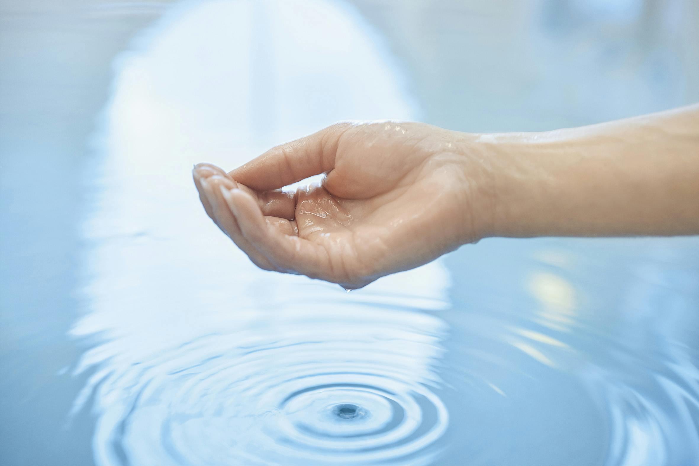 Detailaufnahme einer Hand, die Wasser ins Becken des Thermalbades tropfen lässt.