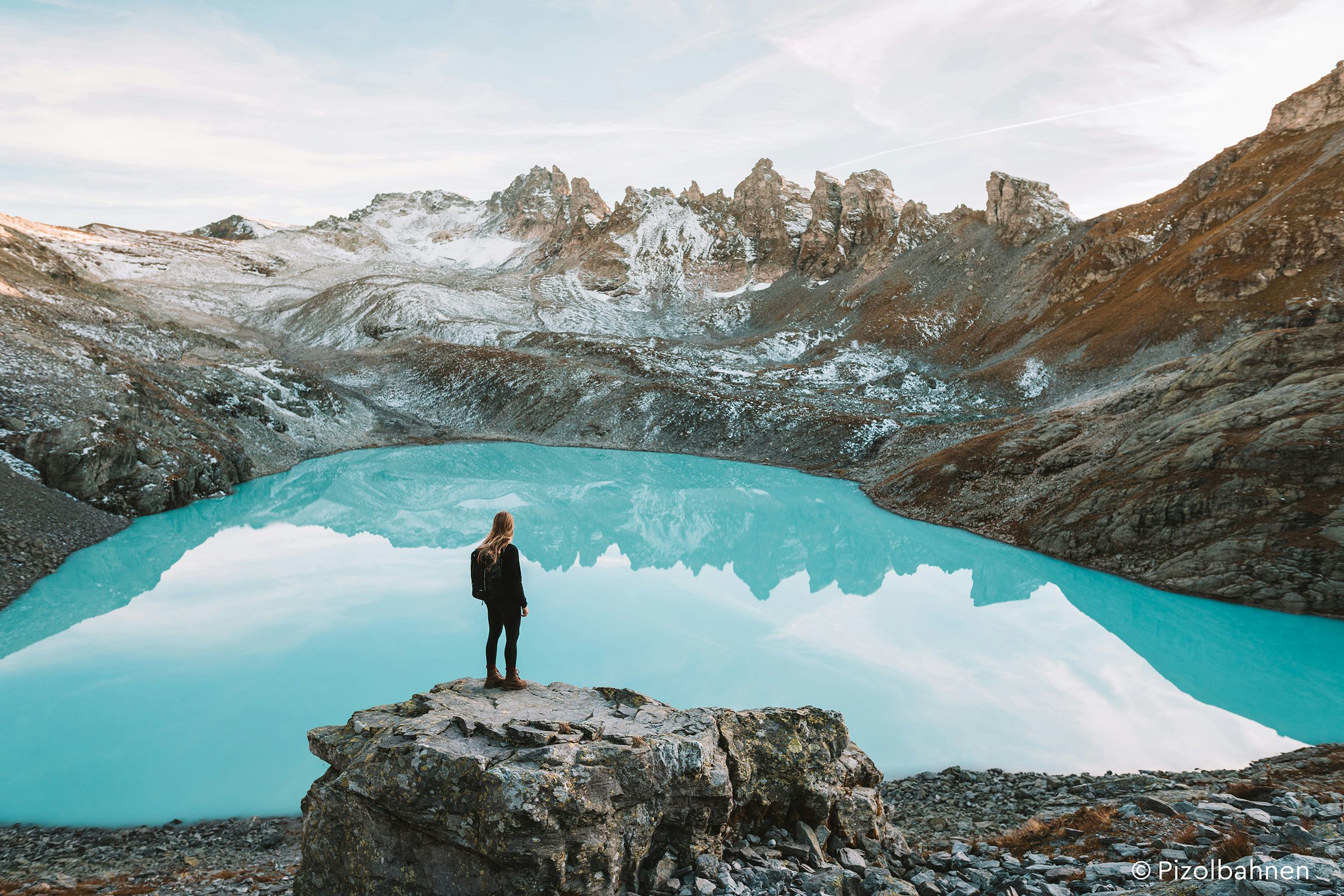 Eine Person steht vor einem türkisblauen See umringt von Bergen.