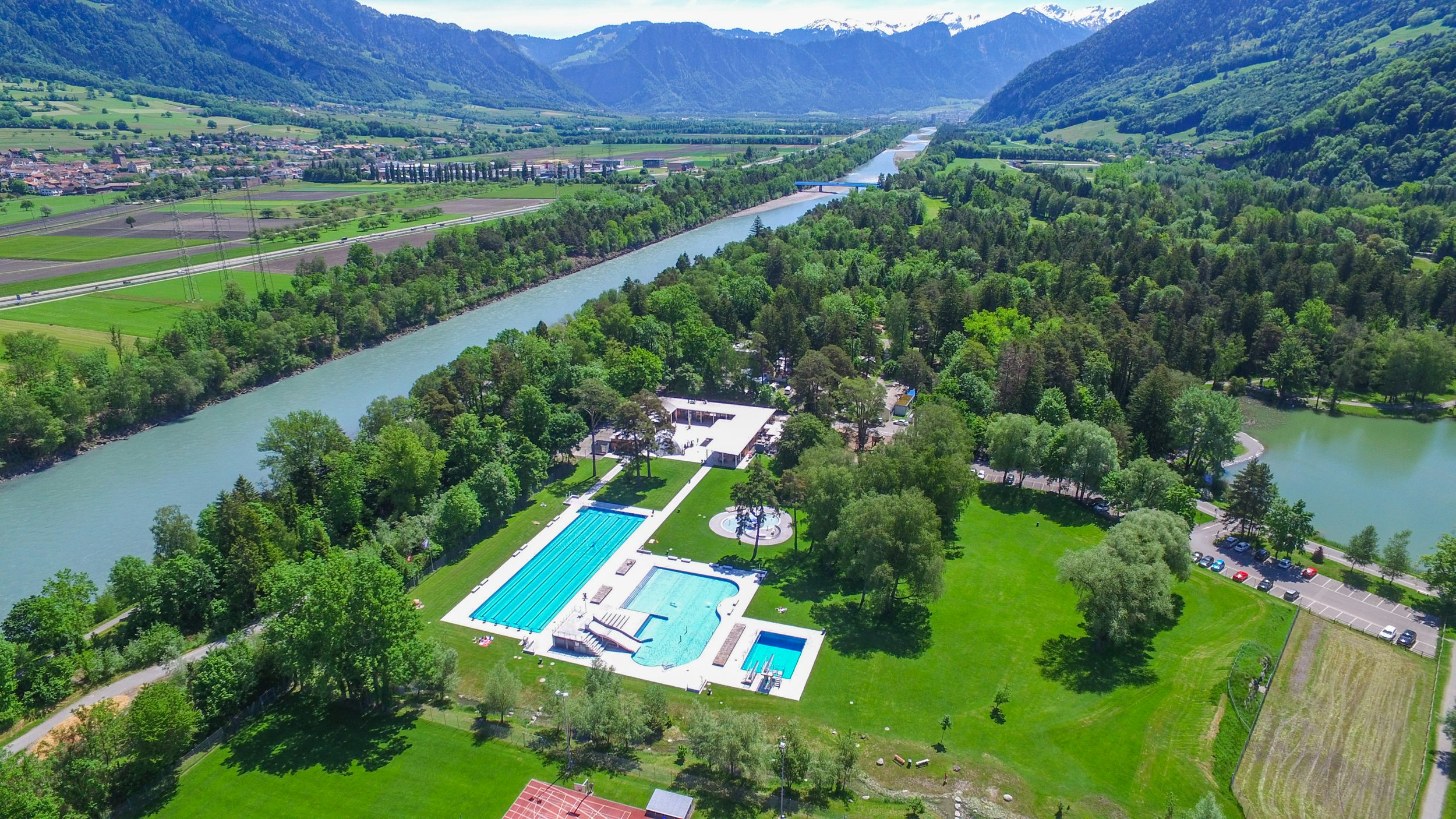 Ein grüner Park mit großem Schwimmbecken aus der Luftperspektive fotografiert.
