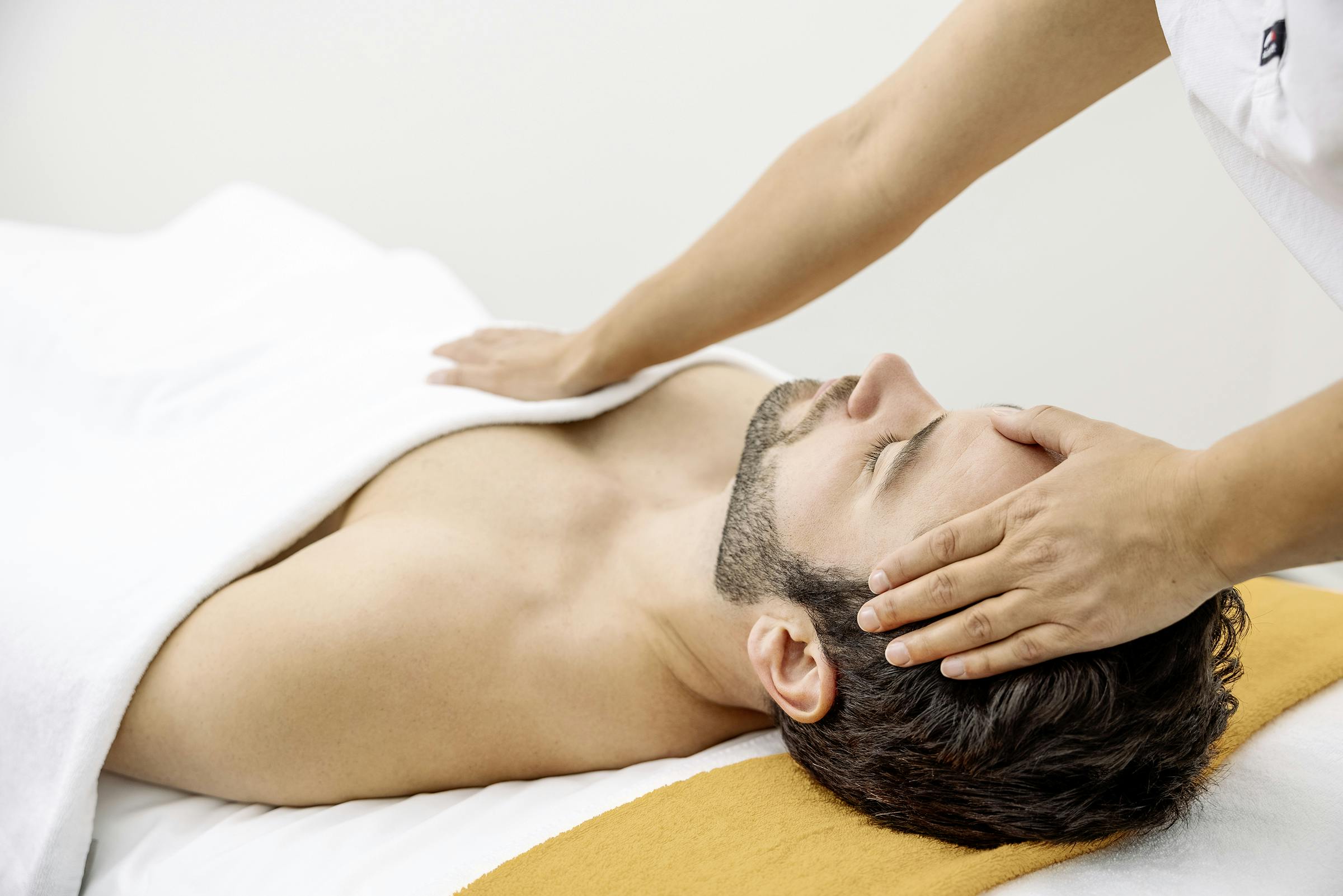 Ein Mann wird vorsichtig von einem Therapeuten am Kopf und an der Brust berührt.
