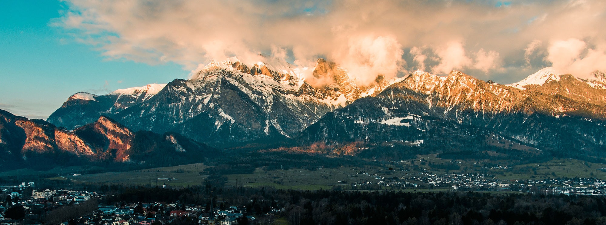 Panoramabild einer Berglandschaft halb mit Schnee bedeckt und von der Sonne angestrahlt.