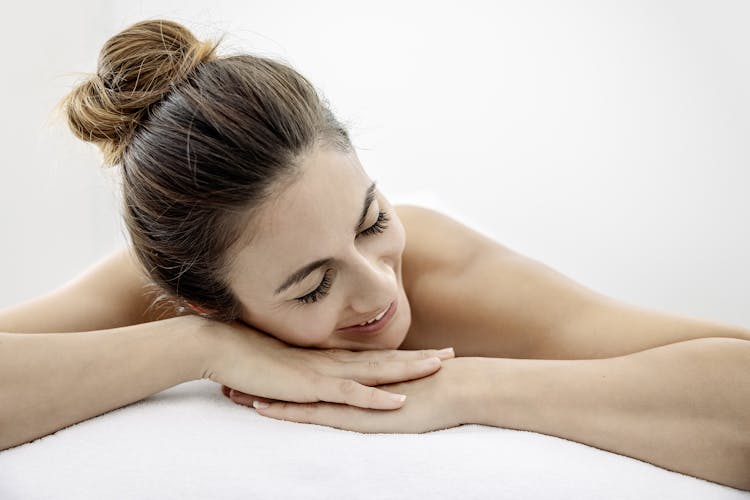 Eine Frau liegt auf einer Massageliege und hat beide Arme vor dem Kopf zusammen gelegt.