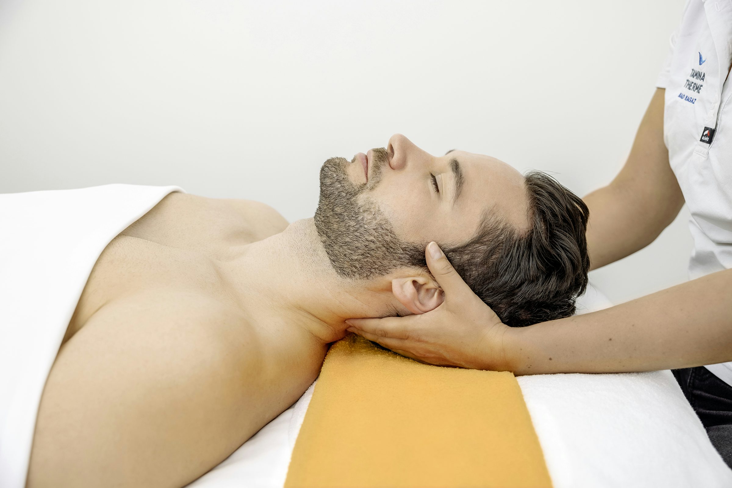 Ein Mann liegt auf einer Massageliege und erhält eine Nackenmassage.