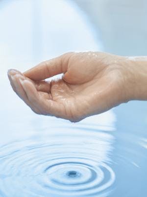 Detailaufnahme einer Hand, die Wasser ins Becken des Thermalbades tropfen lässt.