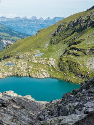 Blick in ein Tal umgeben von Bergen und einem mit türkisfarbenen Wasser gefüllten See.